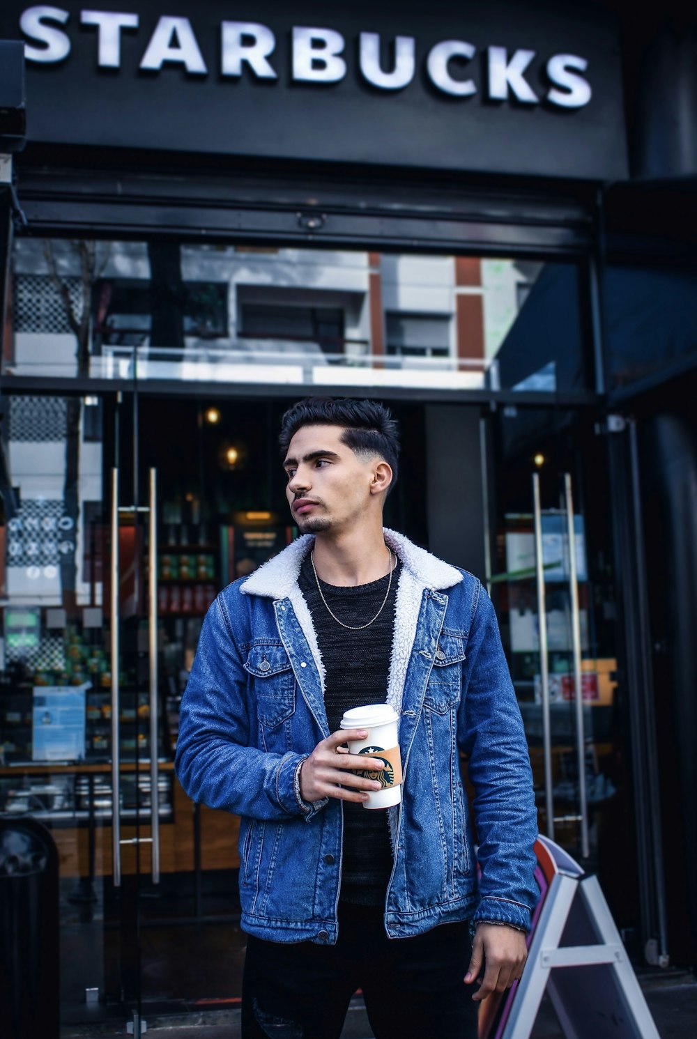 man in blue denim jacket holding white ceramic mug