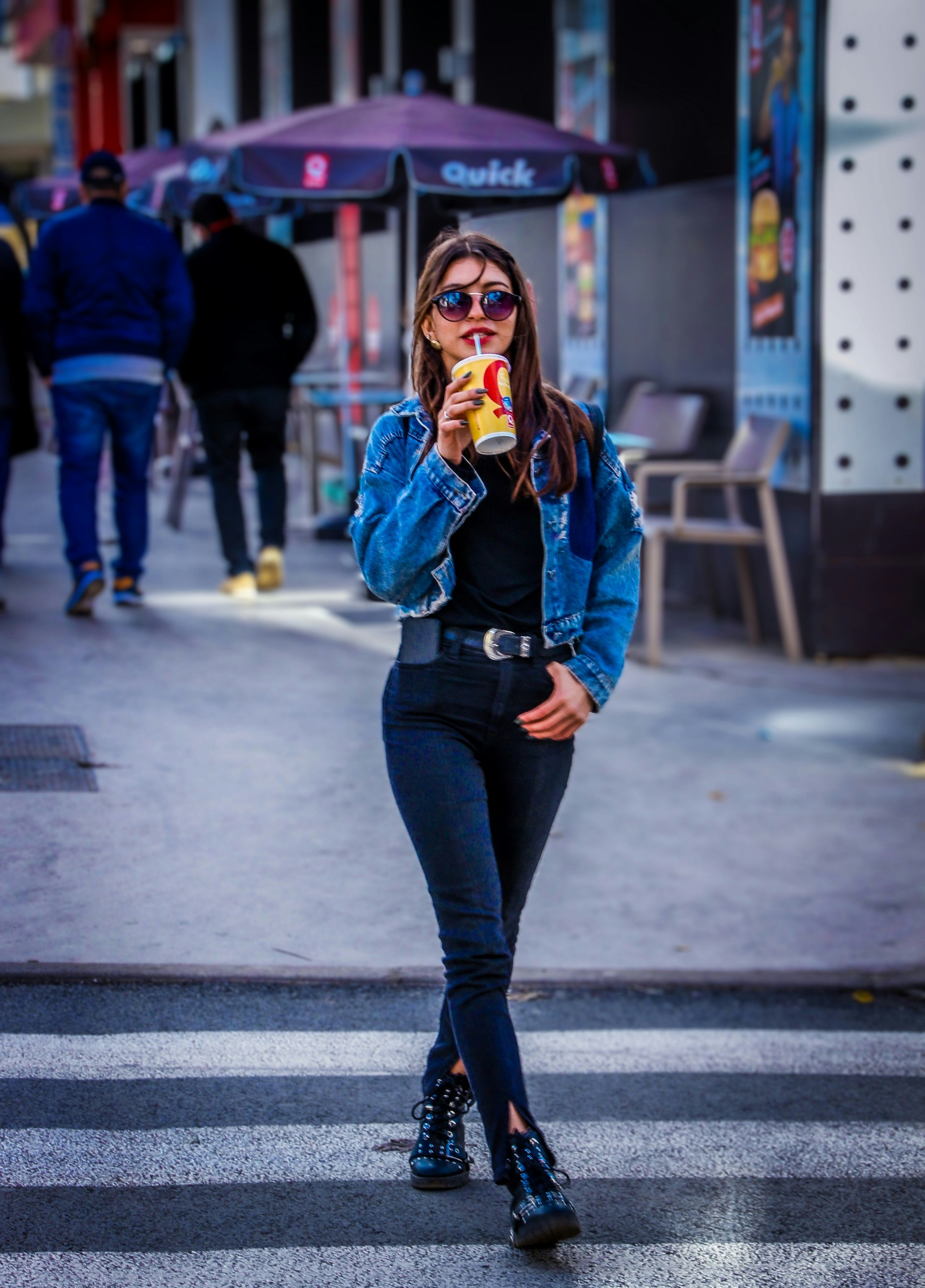 Woman in blue denim jacket and black pants standing on sidewalk during ...
