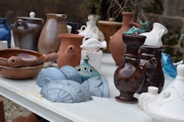 An artistic arrangement of functional ceramic mugs and sculptural vases on a wooden table.