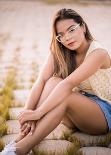 woman in white sleeveless shirt and blue denim shorts sitting on brown rock during daytime