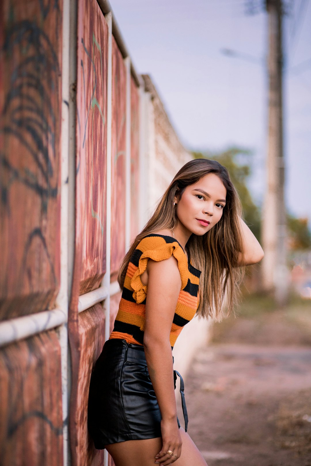 woman in black and orange crop top and black denim shorts standing beside brown wooden wall