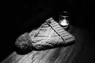 A minimalist black beanie folded neatly next to a steaming mug by the fire.