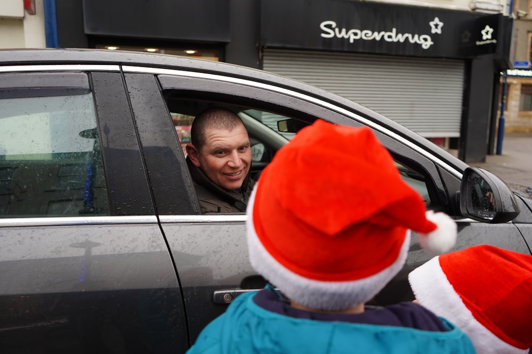 man in blue jacket and red knit cap sitting on car