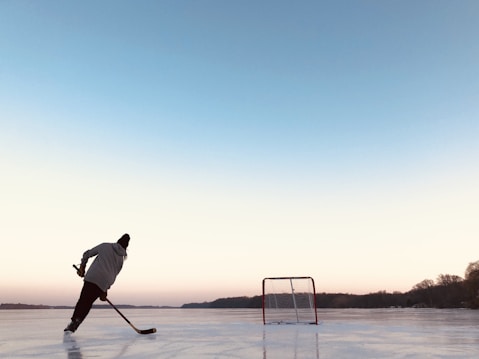 Man playing ice hockey on frozen Bass Lake during sunny winter day.