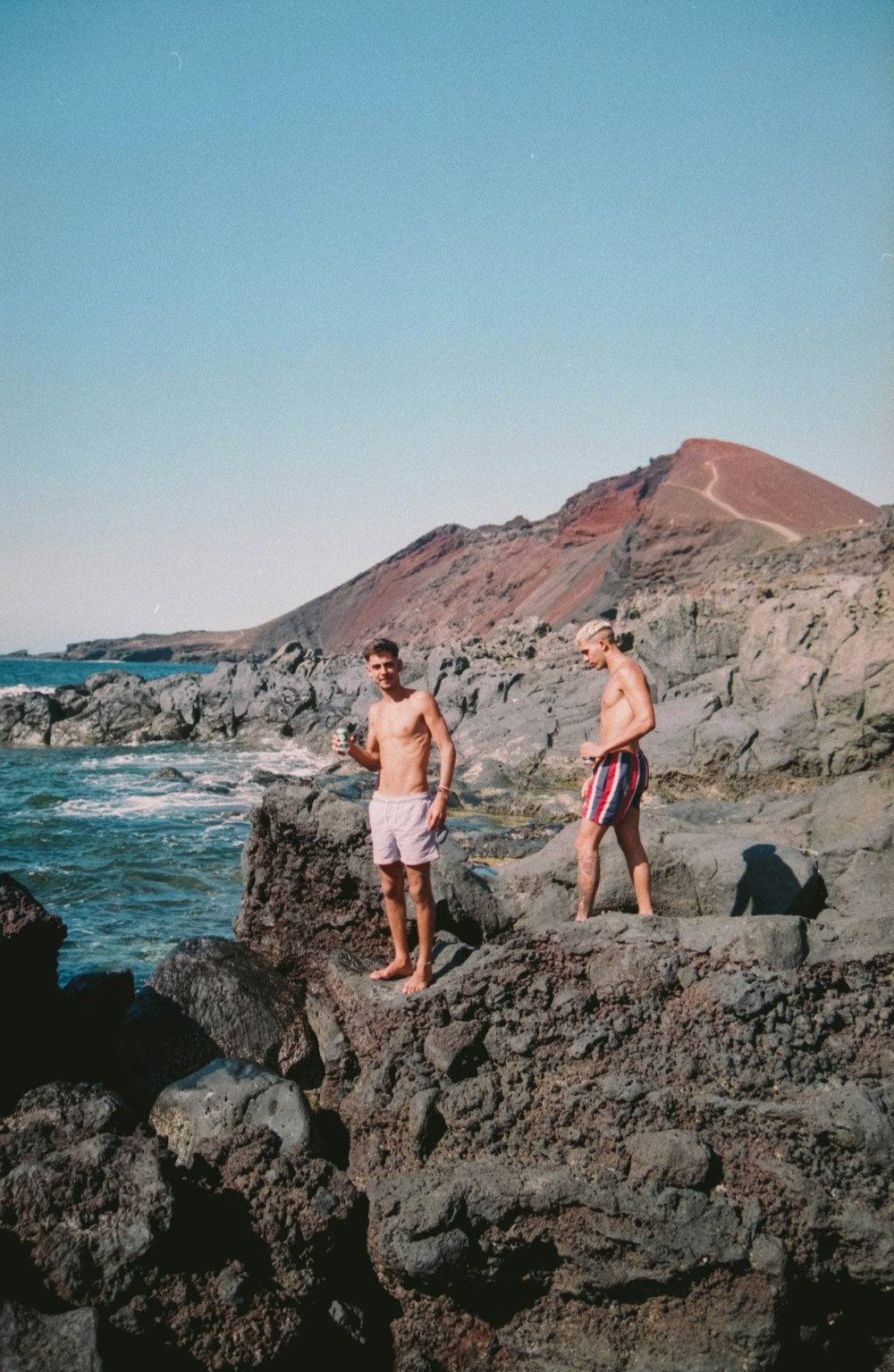 2 men standing on rocky shore during daytime
