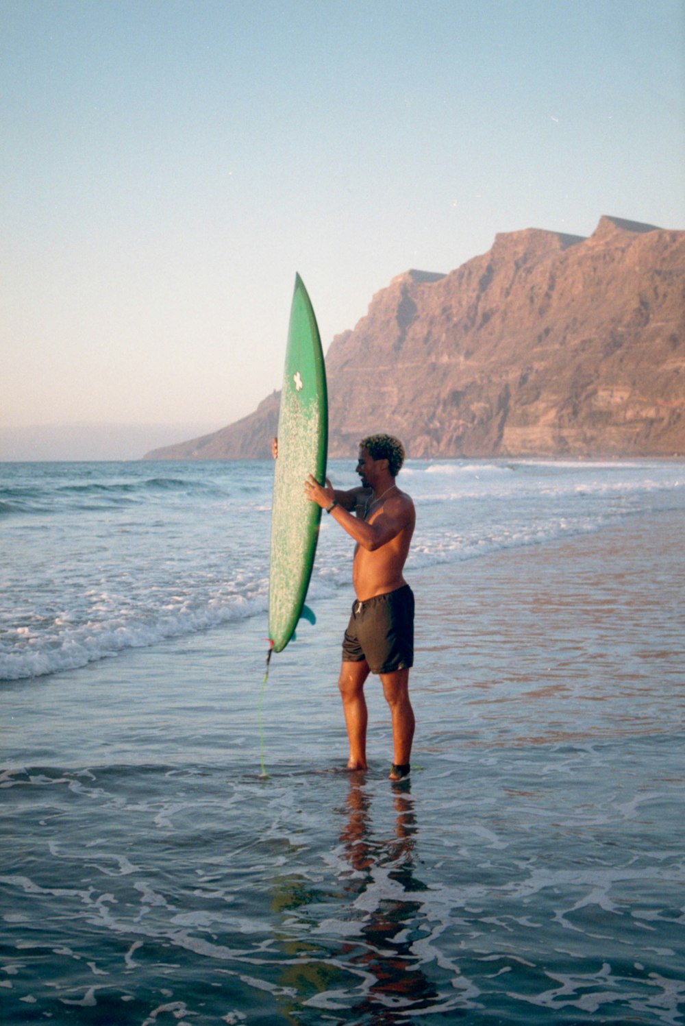 Mujer en bikini negro sosteniendo una tabla de surf verde de pie en la playa durante el día