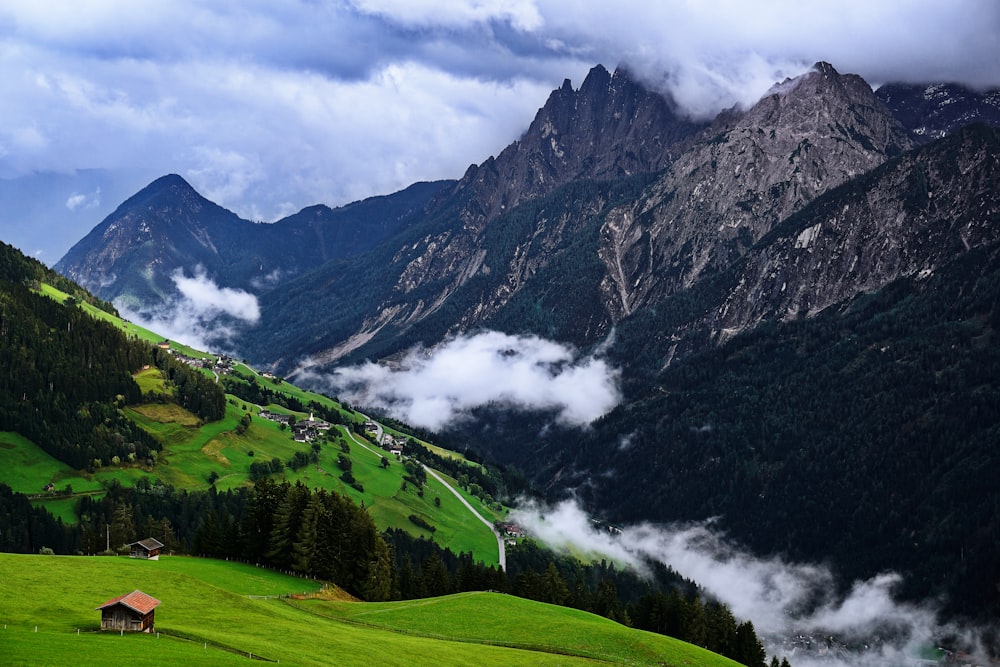 green grass field and mountains under white clouds and blue sky during daytime