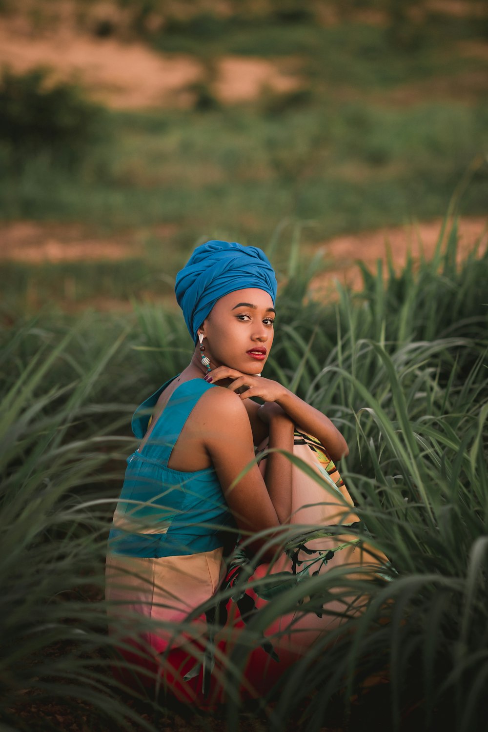 woman in blue and brown floral sleeveless dress sitting on green grass during daytime