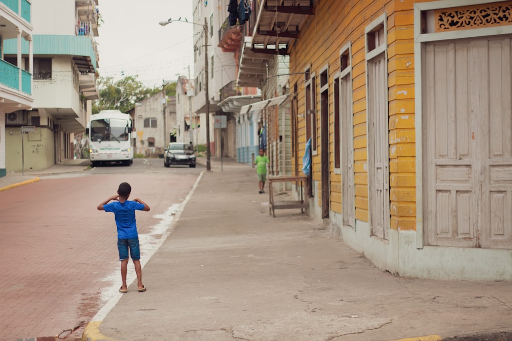 boy in blue t-shirt walking on sidewalk during daytime