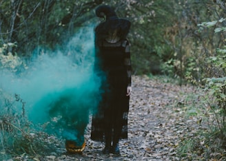 man in black jacket standing on rocky ground near green water