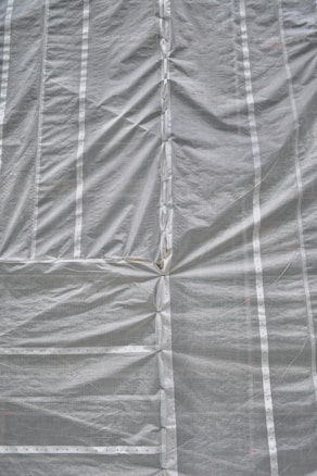 A large sheet of gray construction tarp with vertical and horizontal seams is stretched across the surface. The material appears to have a grid-like texture, with visible creases and folds.