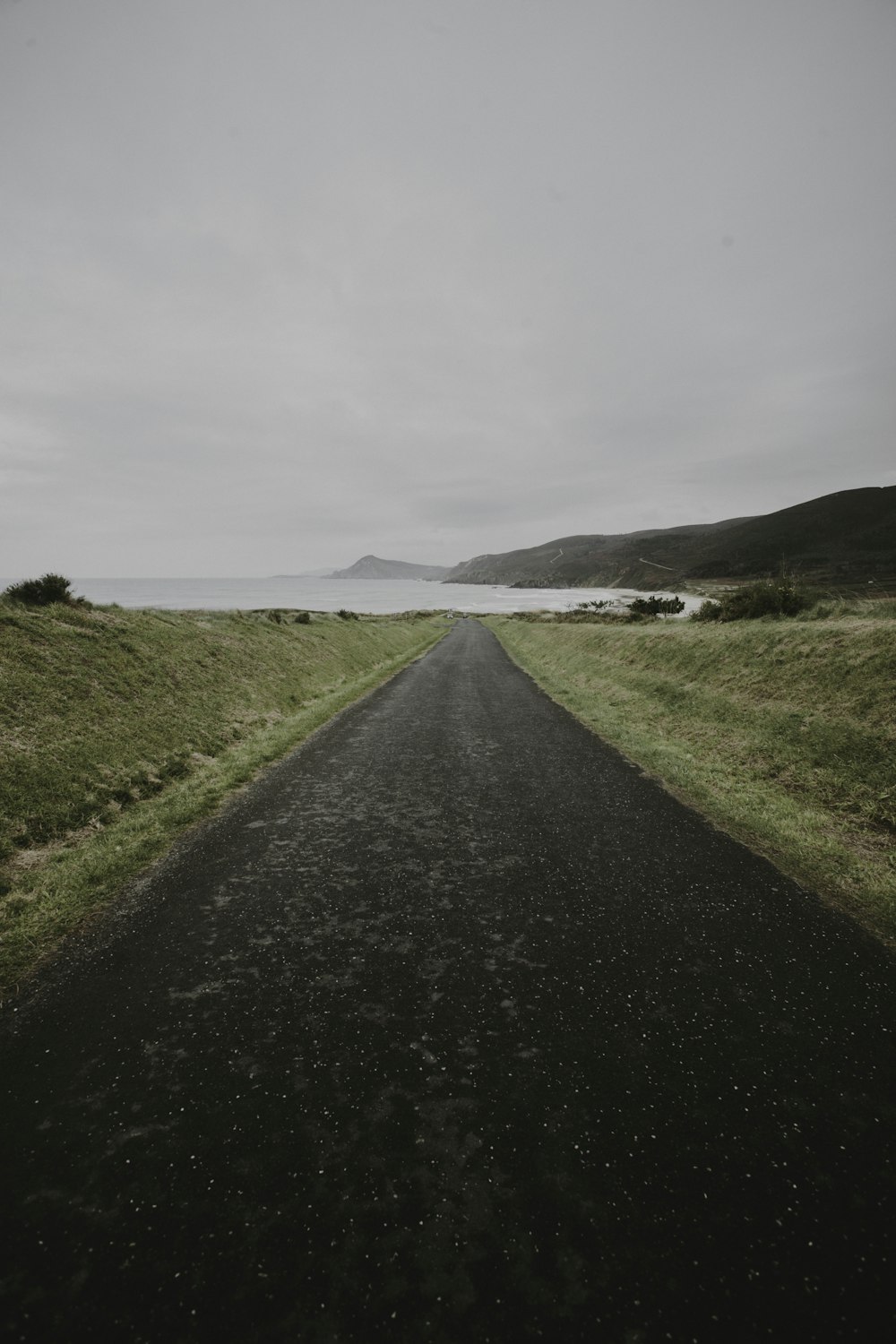 gray asphalt road between green grass field under gray sky during daytime