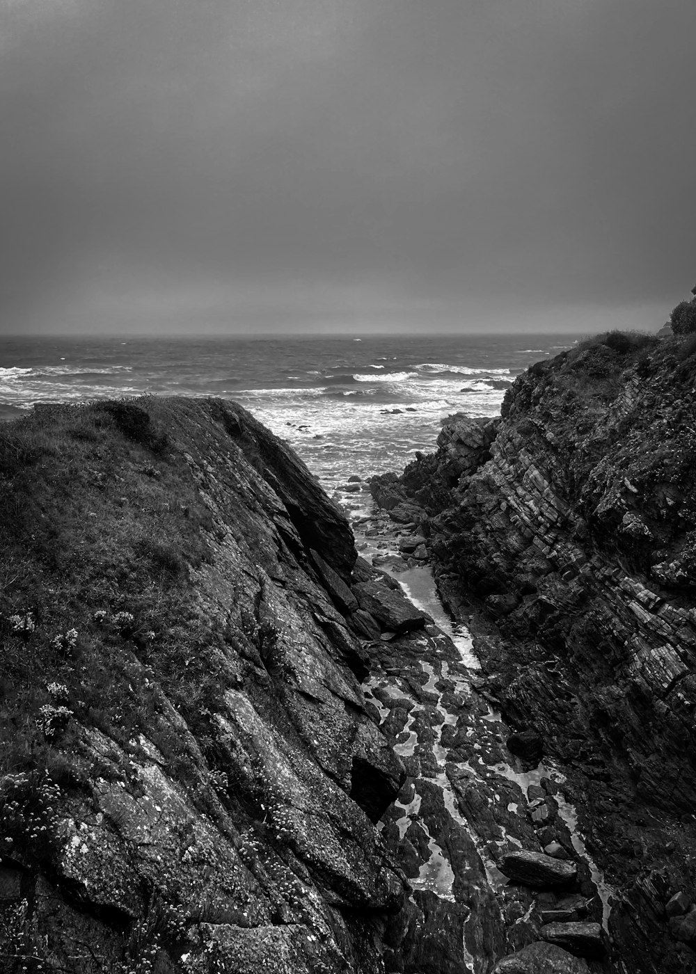 grayscale photo of rocky mountain by the sea