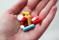 A hand holds a variety of colorful pills and capsules of different shapes and sizes.