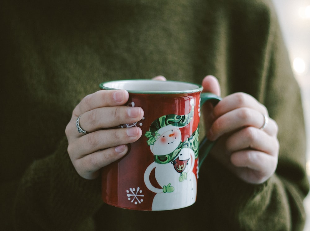 personne tenant une tasse en céramique rouge et blanche