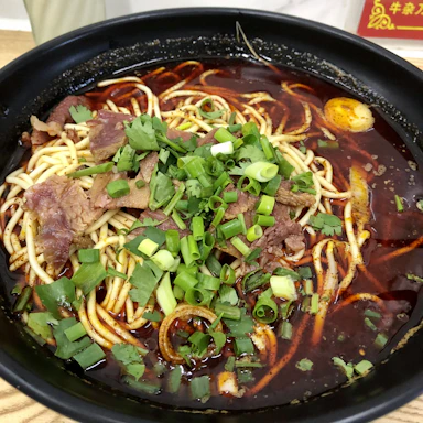 A steaming bowl of hand-pulled beef lamian noodles garnished with fresh herbs and green onions.