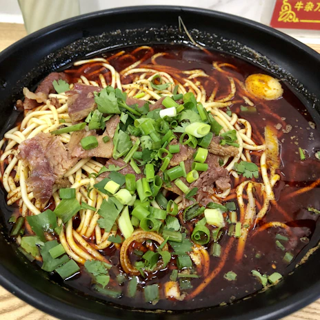 A steaming bowl of hand-pulled noodles topped with fresh vegetables and tender slices of beef.