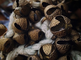 A close-up of a cluster of metallic bells with an intricate pattern, resting on a textured white rope. The bells have a weathered look with visible openings, and they are tightly packed together.