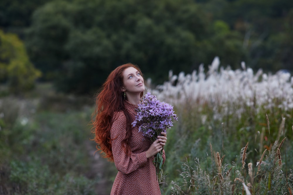 紫色の花を持つ茶色のセーターを着た女性