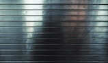 Metallic surface with horizontal grooves, reflecting subtle gradients of light and shadows.