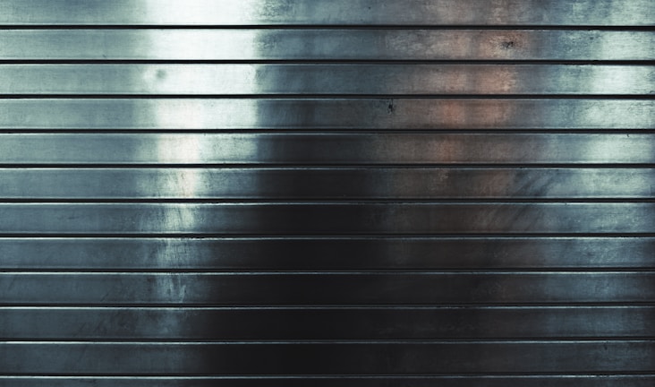 Metallic surface with horizontal grooves, reflecting subtle gradients of light and shadows.
