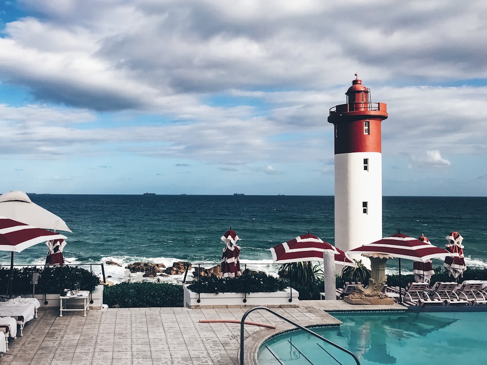 Faro rosso e bianco vicino allo specchio d'acqua durante il giorno