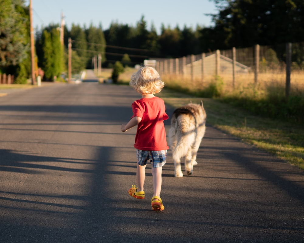 boy in red shirt running on road during daytime