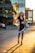 A stylish woman wearing a chic short dress, smiling confidently in an urban setting.