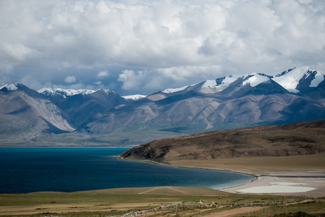 blue body of water near mountain under white clouds and blue sky during daytime