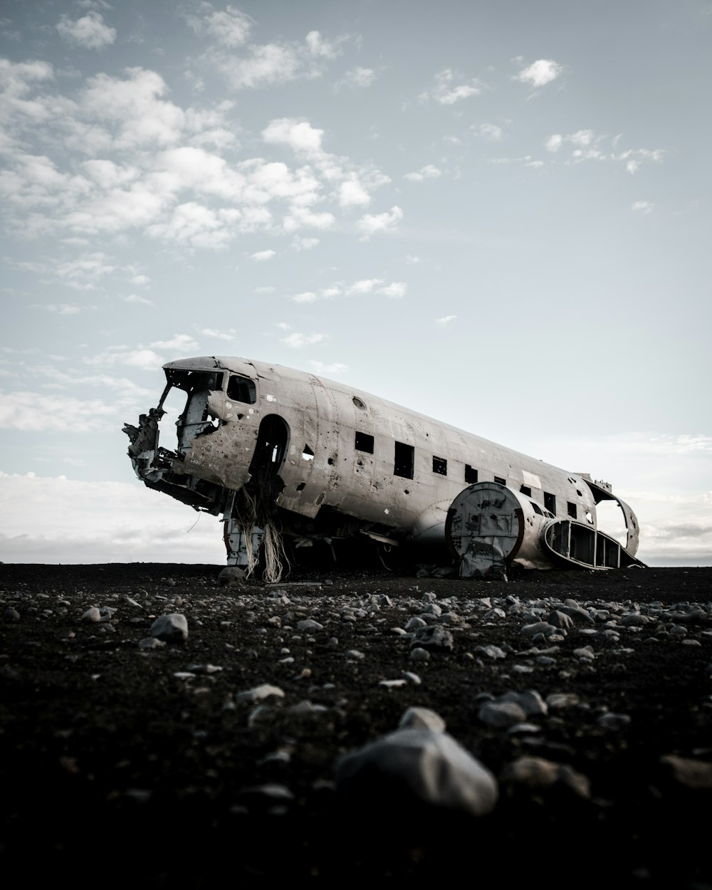 avión destrozado en suelo rocoso gris bajo cielo nublado soleado azul y blanco durante el día