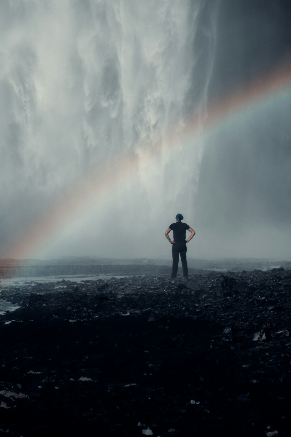 a man standing in the middle of a field with a rainbow in the background