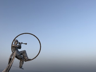 Grande sculpture métallique d'un homme assis jouant de la trompette dans un anneau, contre un ciel