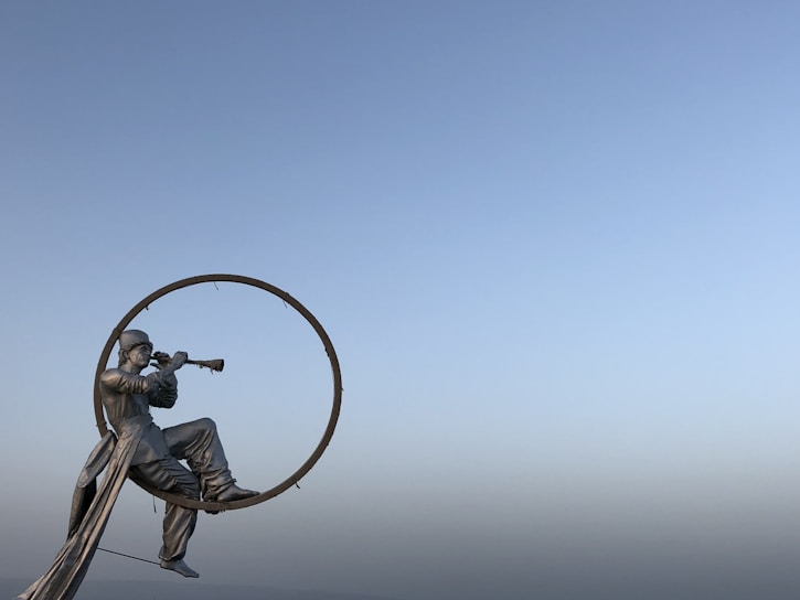Grande sculpture métallique d'un homme assis jouant de la trompette dans un anneau, contre un ciel