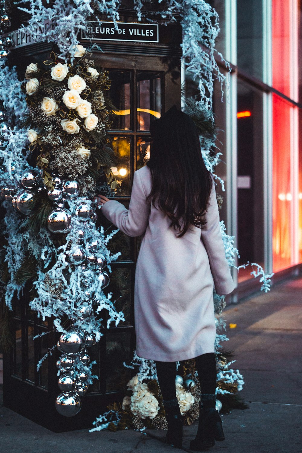 Mujer en abrigo rosa de pie junto al árbol de Navidad