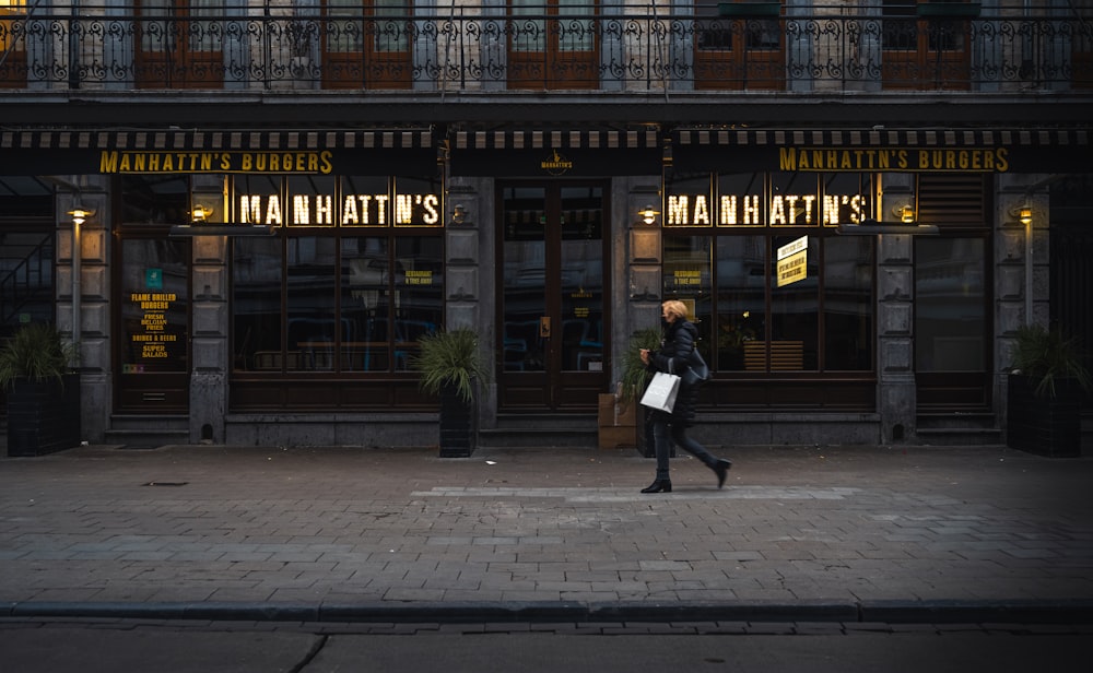 man in black jacket walking on sidewalk in front of brown and black building during daytime