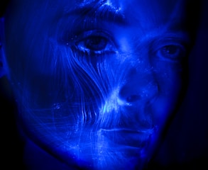 A human-robot hybrid face glowing with neon blue and purple highlights.