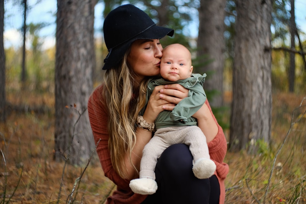 woman in red long sleeve shirt carrying baby in green jacket