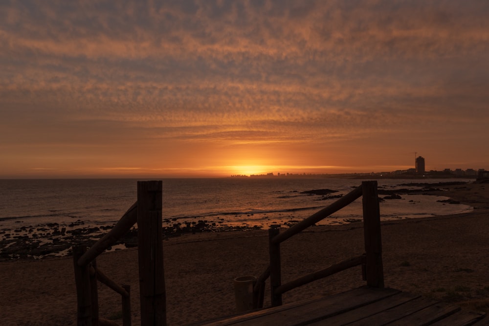 valla de madera marrón en la playa durante la puesta del sol