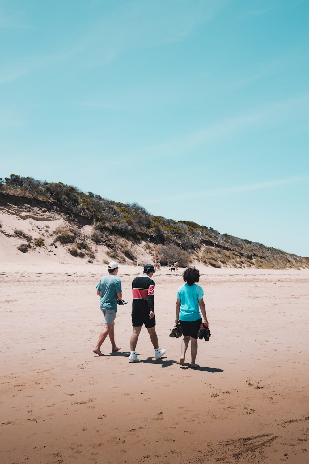 3 people walking on brown sand during daytime