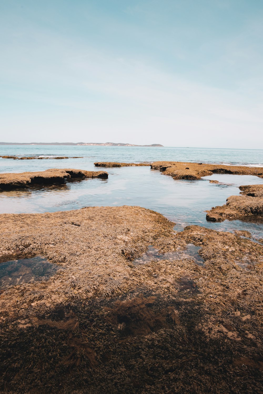 brown and gray rocks on body of water under blue sky during daytime