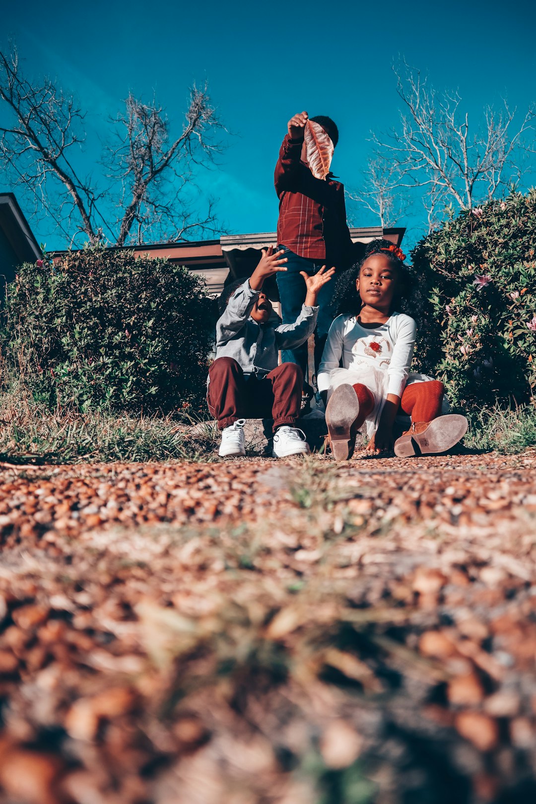 2 boys and girl sitting on ground during daytime