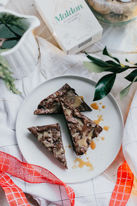 Close-up of rich chocolate brownies with a glossy ganache topping, sprinkled with sea salt flakes on a cream-colored plate.