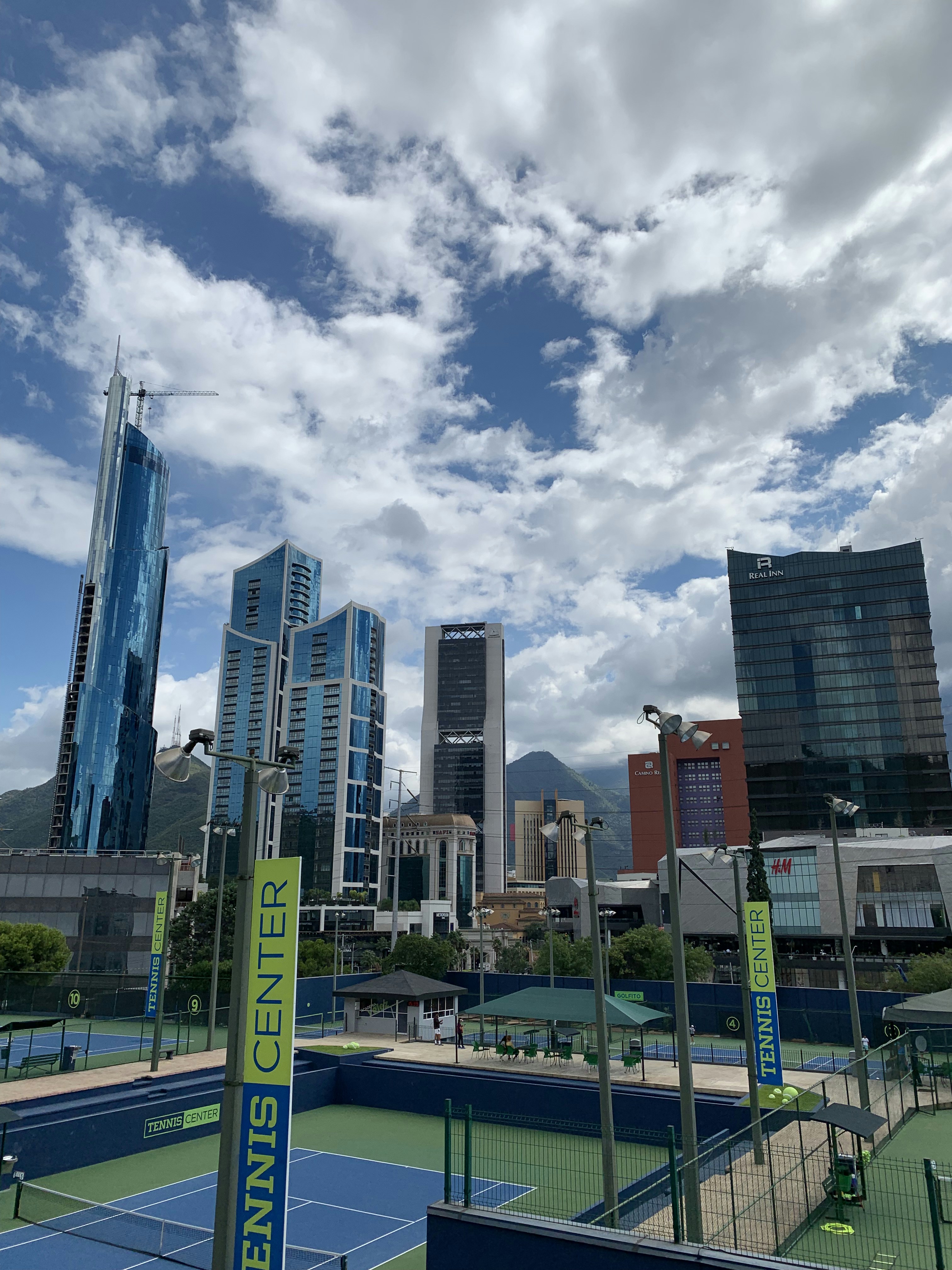Multiple tennis courts at a modern athletic centre with mountain backdrop in clear blue sky