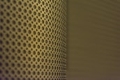 A close-up view of a perforated metal surface with a pattern of evenly spaced circular holes. The lighting casts a shadow that adds depth and creates a gradient effect across the surface.