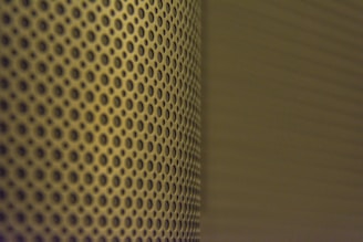 A close-up view of a perforated metal surface with a pattern of evenly spaced circular holes. The lighting casts a shadow that adds depth and creates a gradient effect across the surface.