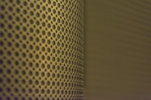 A close-up view of a perforated metal surface with a pattern of evenly spaced circular holes. The lighting casts a shadow that adds depth and creates a gradient effect across the surface.