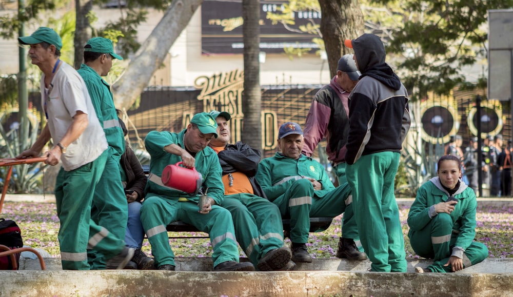 group of men in green and black jackets sitting on concrete bench during daytime