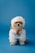 A small dog dressed in a fluffy white costume resembling a mythical creature, holding a tiny gift box with a red ribbon. The background is a solid blue color, creating a playful and whimsical setting.