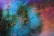 An abstract artwork with swirling colors and dynamic splatters. Vivid blue and green tones blend into shades of purple and red, with scattered dots and streaks of yellow, orange, and black adding texture and movement.
