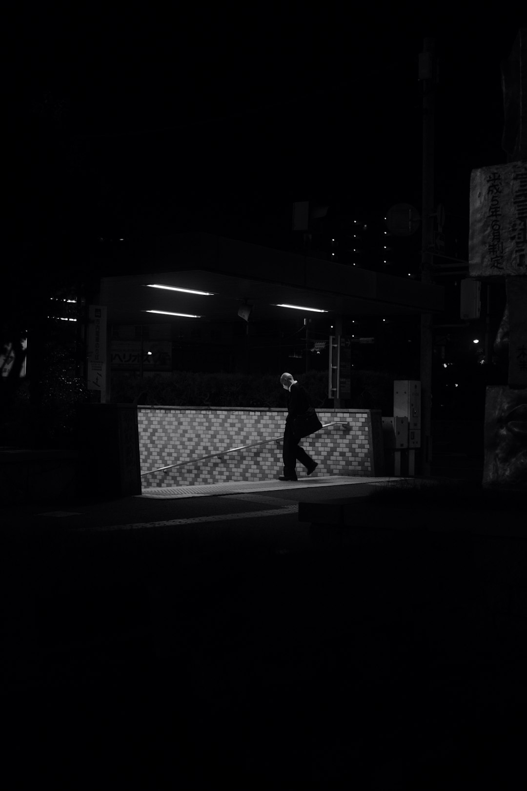 grayscale photo of man in black shirt standing near building